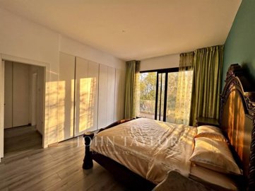 Spacious bedroom with large windows and ample natural light, featuring elegant green curtains and a classic wooden bed frame.