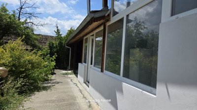 Concrete path leading to entrance door with large windows and garden plants beside the Bulgarian house.
