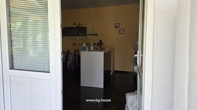 Interior view through open door showing kitchen with white cabinets, black backsplash, and appliances.