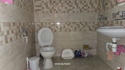 Bathroom featuring beige and brown tiled walls, white toilet, basin, and shower plumbing and fittings.
