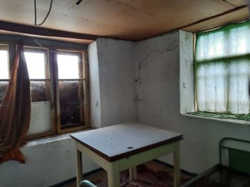 Interior room with white walls, two windows with curtains, and a small table in the center