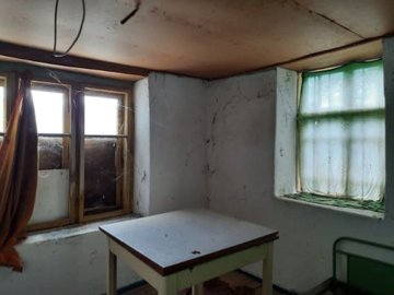Room with white walls, two windows with curtains, and a small table in the middle