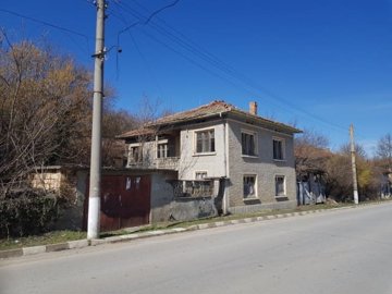 Side perspective showing textured walls, tiled roof, and wooden gates beside the house