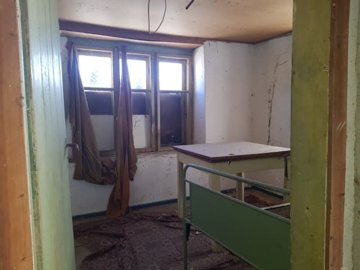 Small room featuring a green metal bed frame, table, barred windows, and curtains