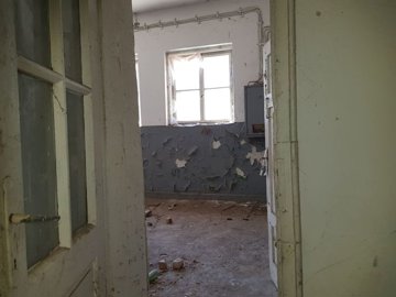 Interior view of a room showing a partially open door and a window with natural light illuminating peeling paint on the walls.