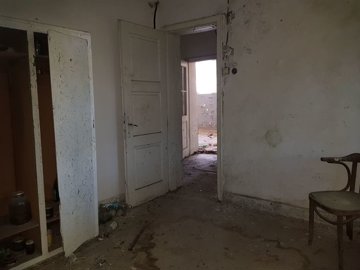 Interior room showing an open door, peeling paint on the walls, and a wooden chair near the corner.