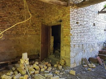 Interior room showing exposed brick walls, an open doorway, and scattered bricks on the floor