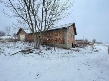 Exterior view of a brick farm building with a metal roof surrounded by snow and bare trees.