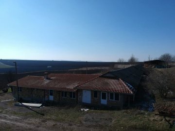 Stone farm building with red tiled roof viewed from above, with expansive fields in the background.