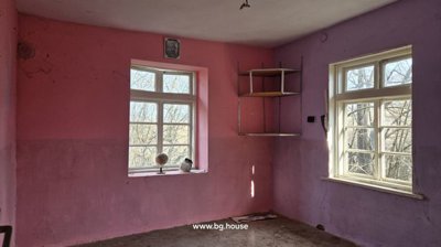 Interior of a room painted pink with two windows providing natural light and a small wall-mounted shelf in the corner