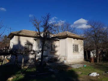 Side view of a single-storey house with a tiled roof and bare trees in the garden area