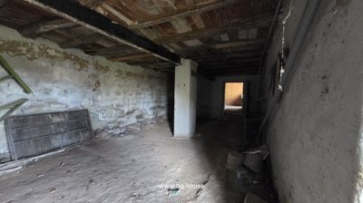 Spacious interior room featuring exposed wooden ceiling beams, rough plaster walls, and a dirt floor with scattered debris.