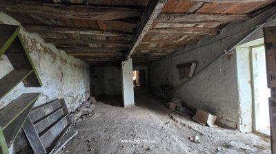 Room interior showing exposed wooden beams on the ceiling, plaster walls, and a dirt floor with some debris and old wooden boards.