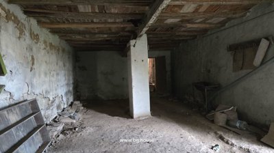 View of an interior room featuring wooden ceiling beams, plaster walls, and a dirt floor with some debris and old wooden boards.