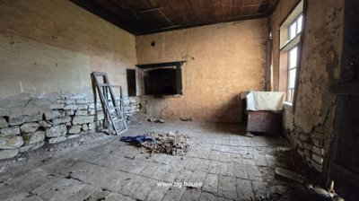 Interior room showing stone lower walls, plaster upper walls, a tiled floor, and a large window letting in natural light.