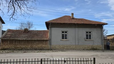 Front exterior view of a stone and brick house with a tiled roof and a brick wall along the street.
