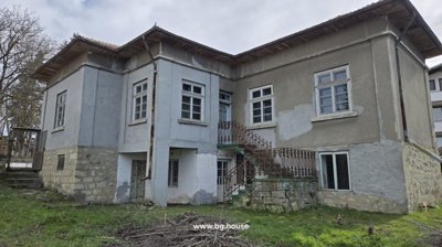 Exterior view of a stone and brick house showing external stairs and multiple windows in a rural area.
