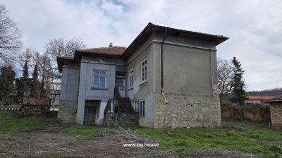Exterior view of a stone and brick house showing external stairs and multiple windows in a rural area.