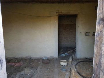 Empty interior room of a farm building showing plastered walls, a dirt floor, and a doorway leading to an adjacent space.