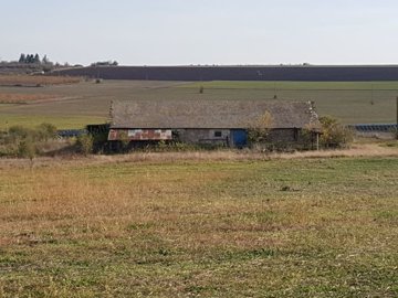 Distant view of the farm building with tiled roof surrounded by open land and fields.