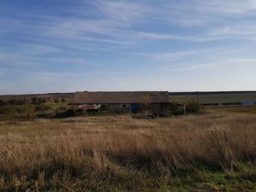 View of the farm building with tiled roof set in grassy countryside with open fields beyond.