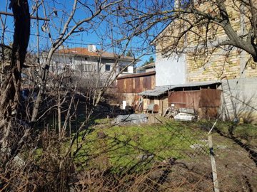 Grassy building land featuring garden beds covered with plastic and surrounding residential buildings