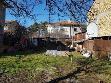 Grassy fenced plot showing garden beds, bare trees, and nearby brick and plaster buildings
