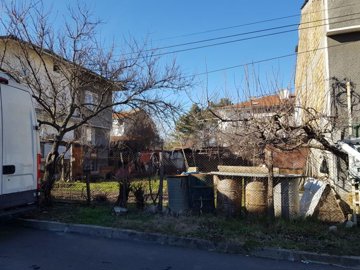 Fenced grassy plot with garden beds, bare trees, and a white van parked on the roadside
