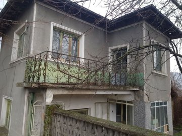 View of the two-storey house corner showing a balcony with decorative green metal railing and multiple windows.