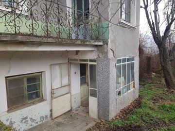 View of the house corner featuring an open door, windows, and garden greenery around the building.