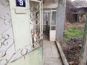 Metal entrance gate partially open leading to a tiled pathway and the front door of the house.