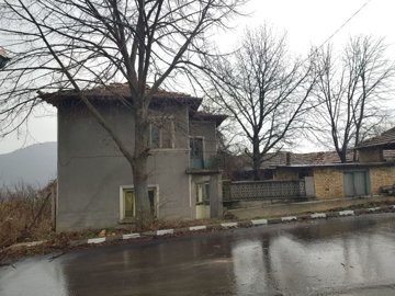 Side perspective of the two-storey house with visible balcony and bare trees on a rainy day