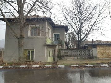 Exterior view of the two-storey house with balcony and bare trees on a rainy day