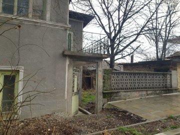 View of the entrance gate and paved path leading to the two-storey house with balcony