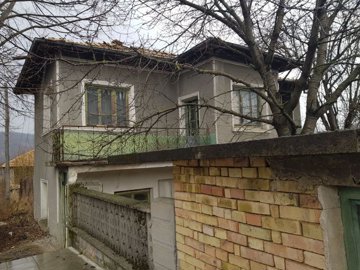 View of the two-storey house with balcony behind a brick wall and bare trees