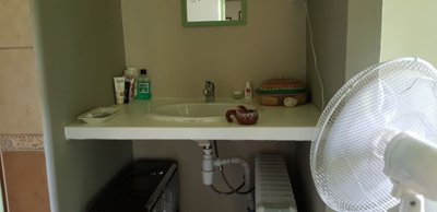 Bathroom basin set in a niche with mirror above, various toiletries on the counter, and a fan and heater positioned below.