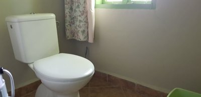 White toilet positioned near a window with floral curtain, set on a tiled floor.