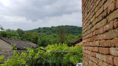 Green forested hills and village rooftops seen from beside the brick wall of the house.