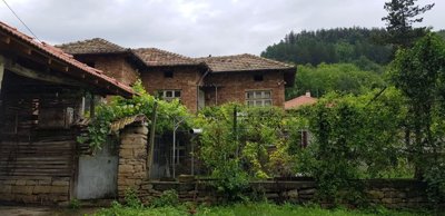 View of a brick house with tiled roof behind a garden area and stone wall, under a cloudy sky.
