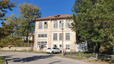 Front view of the three-level former school building showing weathered facade and surrounding trees