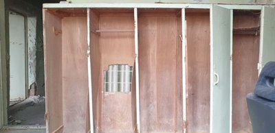 Room containing wooden wardrobes with visible damage and peeling paint