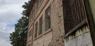Close-up view of the facade of an old stone building with peeling plaster and several windows under a cloudy sky.