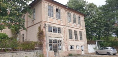 View of the building showing weathered walls, windows, and nearby vegetation