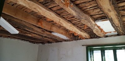 Close-up view of exposed wooden ceiling beams in a room with white walls and a green-framed window.