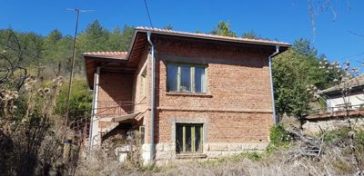 Side view showing green window frames and tiled roof of the brick house in a rural area