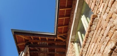 Close-up detail of the tiled roof and metal guttering on the brick house against a blue sky