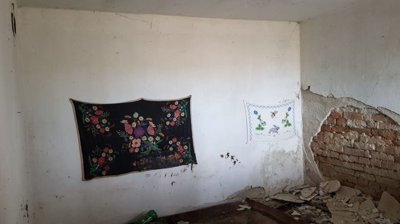 Interior room showing white walls with floral tapestries and an exposed brick section with debris on the floor.