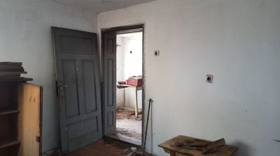 Interior room featuring a grey door open to another room, with wooden furniture and scattered items.