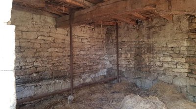 Inside view of a stone outbuilding showing wooden ceiling beams and metal poles supporting the structure, with straw covering the floor.