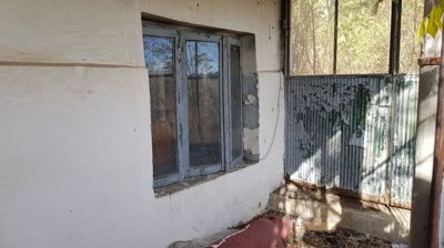 Close-up of a window and a metal door on a white wall showing peeling paint and sunlight shadows.